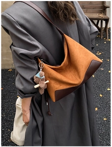 Brown suede and leather hobo bag with a plush bear charm worn by a model in autumn setting