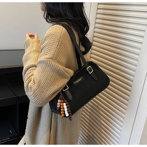 Détail du sac baguette noir minimaliste avec breloque en perles et plaque logo en métal
