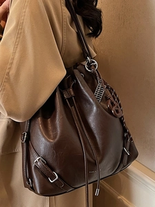 Vintage dark brown drawstring bucket bag made of glossy leather worn with a trench coat