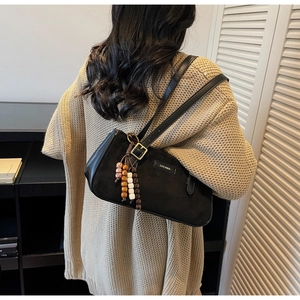 Détail du sac baguette en daim noir avec des perles en bois et une boucle logo
