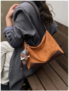 Brown suede underarm shoulder bag with teddy bear pendant shown on model in outdoor setting