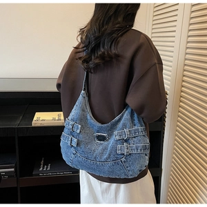 Detail of blue denim shoulder bag with metal plate and decorative buckle straps
