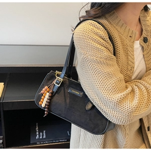 Détail d'un sac baguette noir mat avec pompon en perles de bois et logo métallique