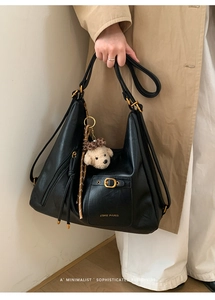 Detail of black matte leather tote bag with gold buckle pocket and dog plush charm