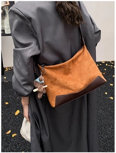Brown suede hobo bag with leather corners and plush bear charm shown on a model