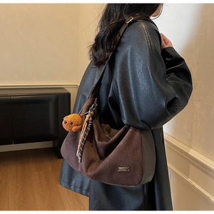 Détail du sac hobo en daim marron avec breloque ours en peluche et pompon tissé