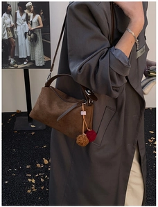 Detail of vintage brown suede shoulder bag with plush ball charm on a grey coat model
