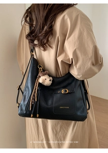 Detail of black faux leather tote bag with plush bear charm and metallic buckle closure