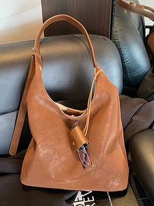 Brown leather large hobo tote bag with shoulder strap and chic glasses charm on sofa