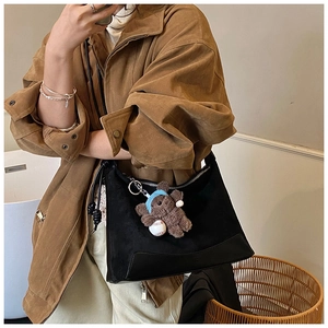 Close-up detail of a black suede shoulder bag with a cute brown teddy bear plush charm