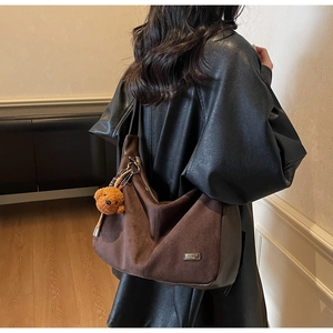 Détail du sac cabas en daim marron foncé avec un pendentif chien en peluche sur un manteau
