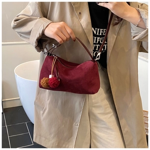 Detail of burgundy suede shoulder bag featuring a decorative pom-pom pendant and slim strap