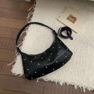 Detailansicht der schwarzen sichelförmigen Ledertasche mit silbernen Nieten auf dem Teppich