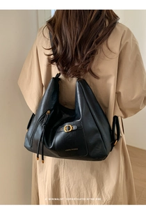 Rear view of a model wearing the large black leather tote bag with gold metal buckles