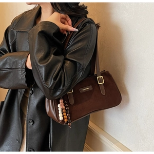 Détail du sac baguette en daim marron avec sangles en cuir et pendentif en perles décoratif