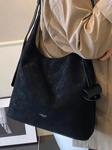 Large black textured leather tote bag worn by a model in a minimalist modern room