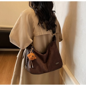 Détail du sac cabas en daim marron foncé avec un porte-clé ours en peluche sur la bandoulière