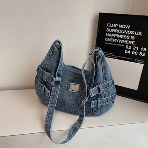 Detail shot of blue denim crossbody bag showing side buckles and metal plate on textured surface