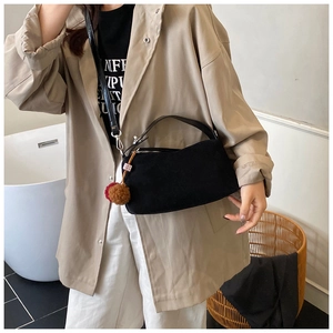 Detail of minimalist black underarm bag featuring a plush charm on a model in a beige trench coat