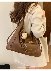 Close-up of brown leather tote bag with functional front pocket and cute bear charm