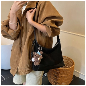 Detail of black suede shoulder bag featuring a cute brown plush bear charm and sleek leather base