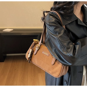 Détail du sac baguette en daim marron chaud avec pendentif à pompon perlé