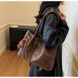 Detail of dark brown leather tote bag with a decorative buckle and plush bear charm