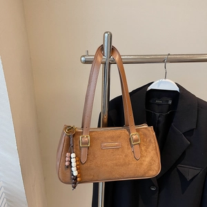 Gros plan d'un sac baguette en daim marron avec boucles dorées et pendentif perlé