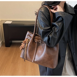 Detail of dark brown vintage tote bag with thin shoulder strap and bear charm accessory