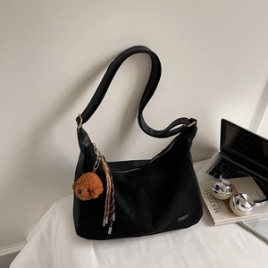 Détail du sac Hobo en toile noire avec breloque chien et pompon sur un bureau élégant