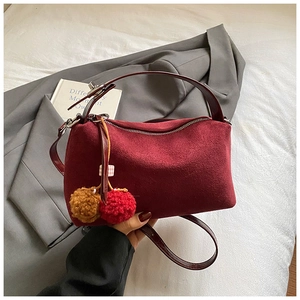 Detailed close-up of burgundy suede underarm bag with decorative colorful plush pom-poms