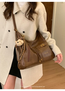 Detail of a large brown leather tote bag with side zippers and a cute bear charm