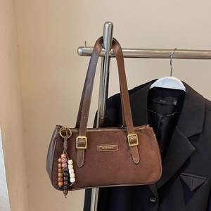 Détail du sac baguette en daim marron foncé avec logo en métal doré et pendentif perlé