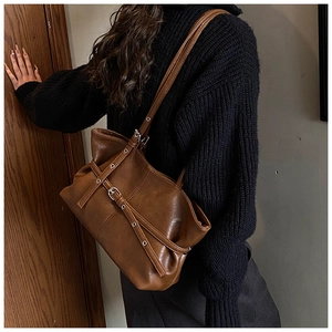 Detail view of retro brown tote bag with leather straps and metal buckle on a shoulder