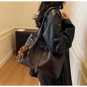 Detail of dark brown leather tote bag with silver buckle and plush bear charm accessory