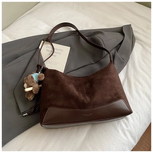 Close-up of brown suede shoulder bag with leather base, logo embossment and plush bear charm