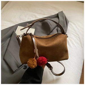 Brown frosted leather underarm bag with decorative plush charms on a neutral bedding background