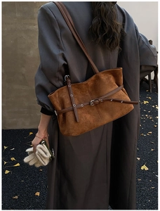 Detail of a brown suede tote bag with parallel decorative straps and metal buckles