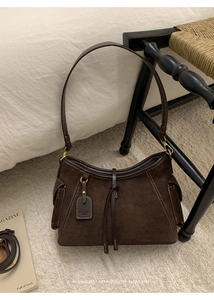 Detail einer dunkelbraunen Wildleder-Schultertasche mit Kontrastnähten und Lederanhänger