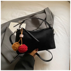Detail of minimalist black matte shoulder bag with a decorative plush pom-pom keychain charm