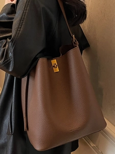 Sac seau en cuir grainé marron avec boucle dorée porté par un mannequin au look chic