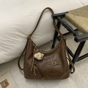 Detail of dark brown leather hobo bag with gold buckle, brand logo and bear charm