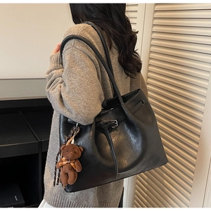 Detail of black leather tote bag featuring a cute brown plush bear charm and metallic buckle