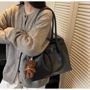 Detail of black faux leather tote bag with silver buckle and brown teddy bear charm