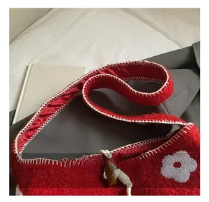 Close-up of red plush tote bag featuring white floral embroidery and whipstitch details