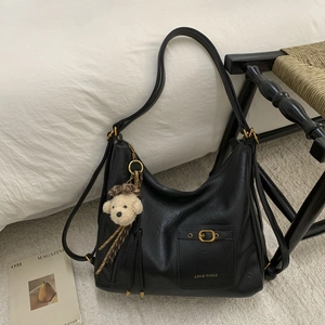 Detail of black leather tote bag featuring antique bronze buckle and bear charm accessory