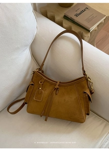 Detailansicht der braunen Wildledertasche mit Tragegriff und Ziernähten auf weißem Sofa