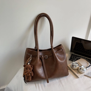 Detail of vintage brown tote bag with metal buckle, plush bear charm, and soft texture