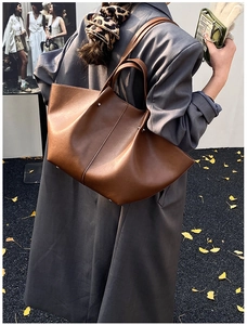 Detailed view of brown leather large capacity bat-shaped tote bag worn with a gray blazer