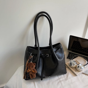Detail view of black leather tote bag with long handles and a cute brown bear pendant
